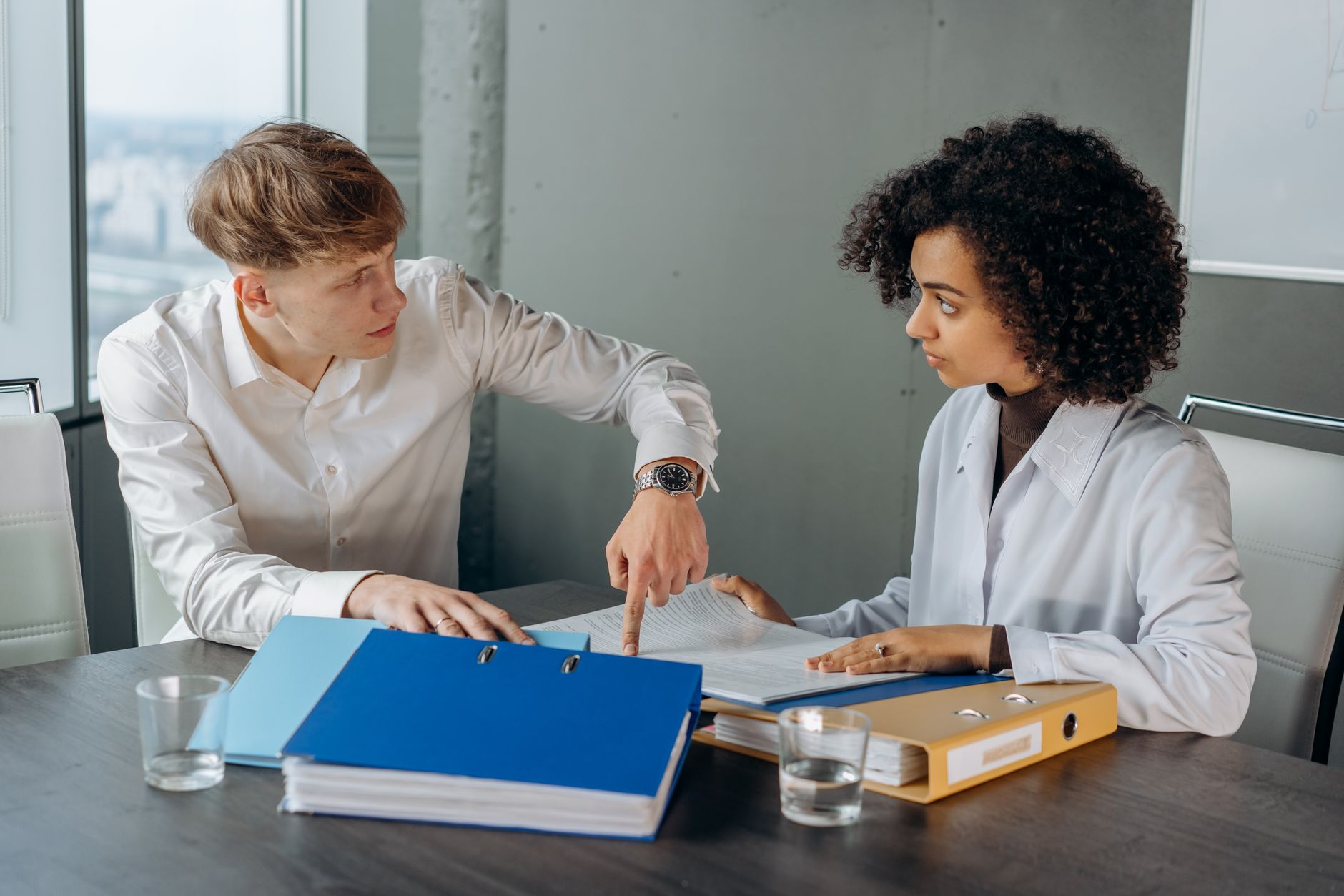 Two colleagues at a meeting table working through a document together, ring binders open in front of them.