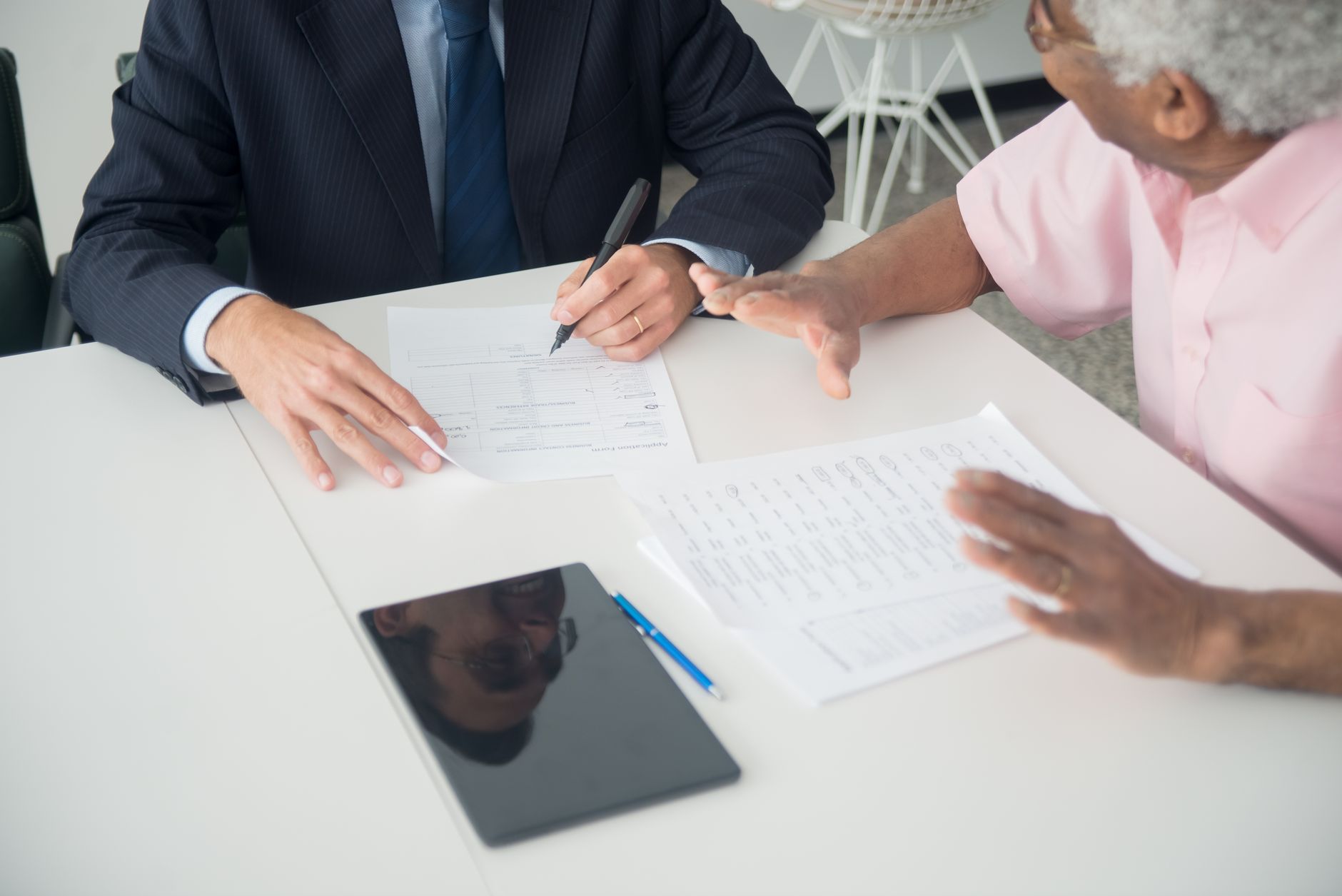 Two people seated at a table completing an application form, a second document set beside it.